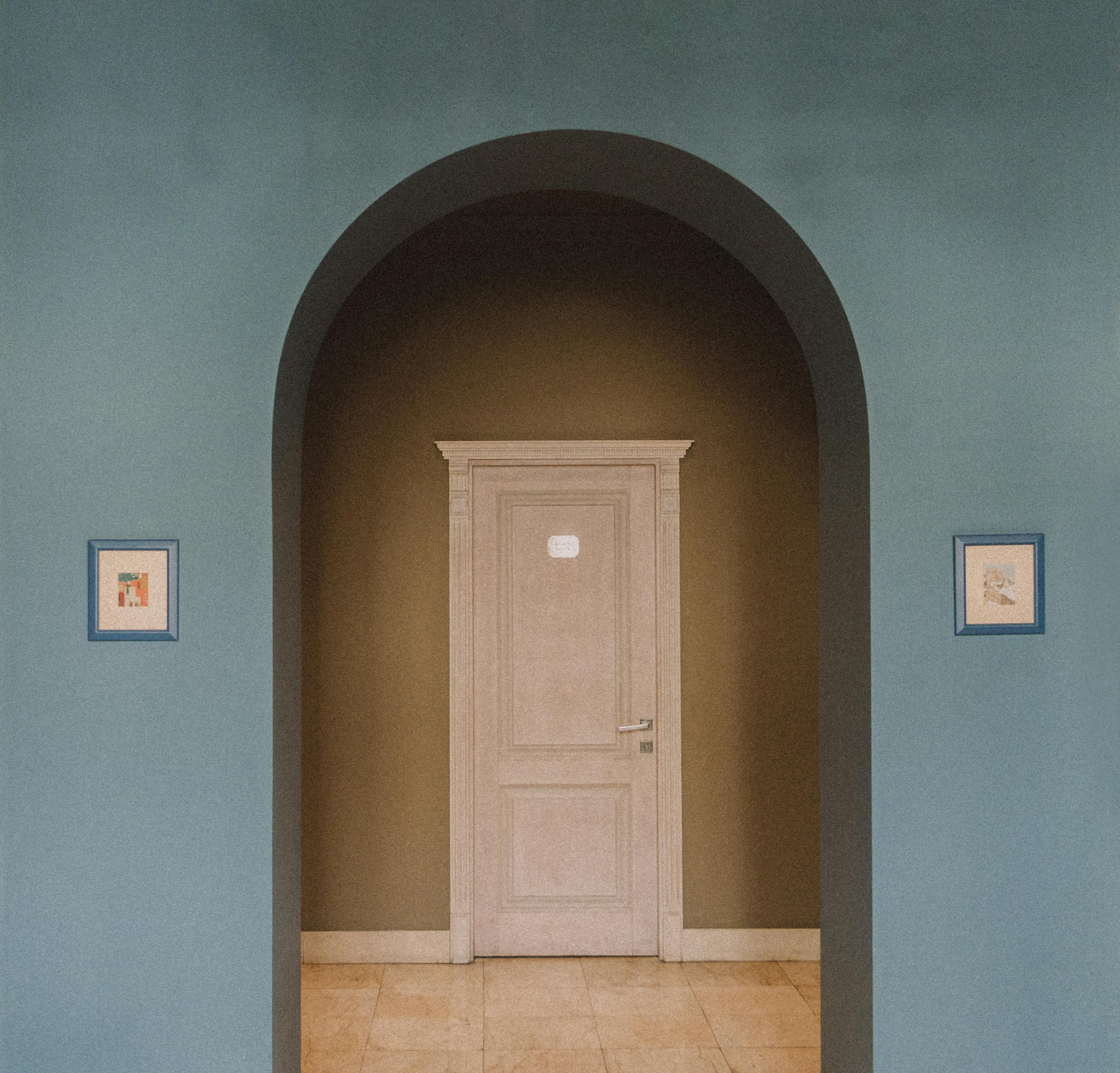 Interior focus on an archway leading to a classic door, flanked by framed artwork.