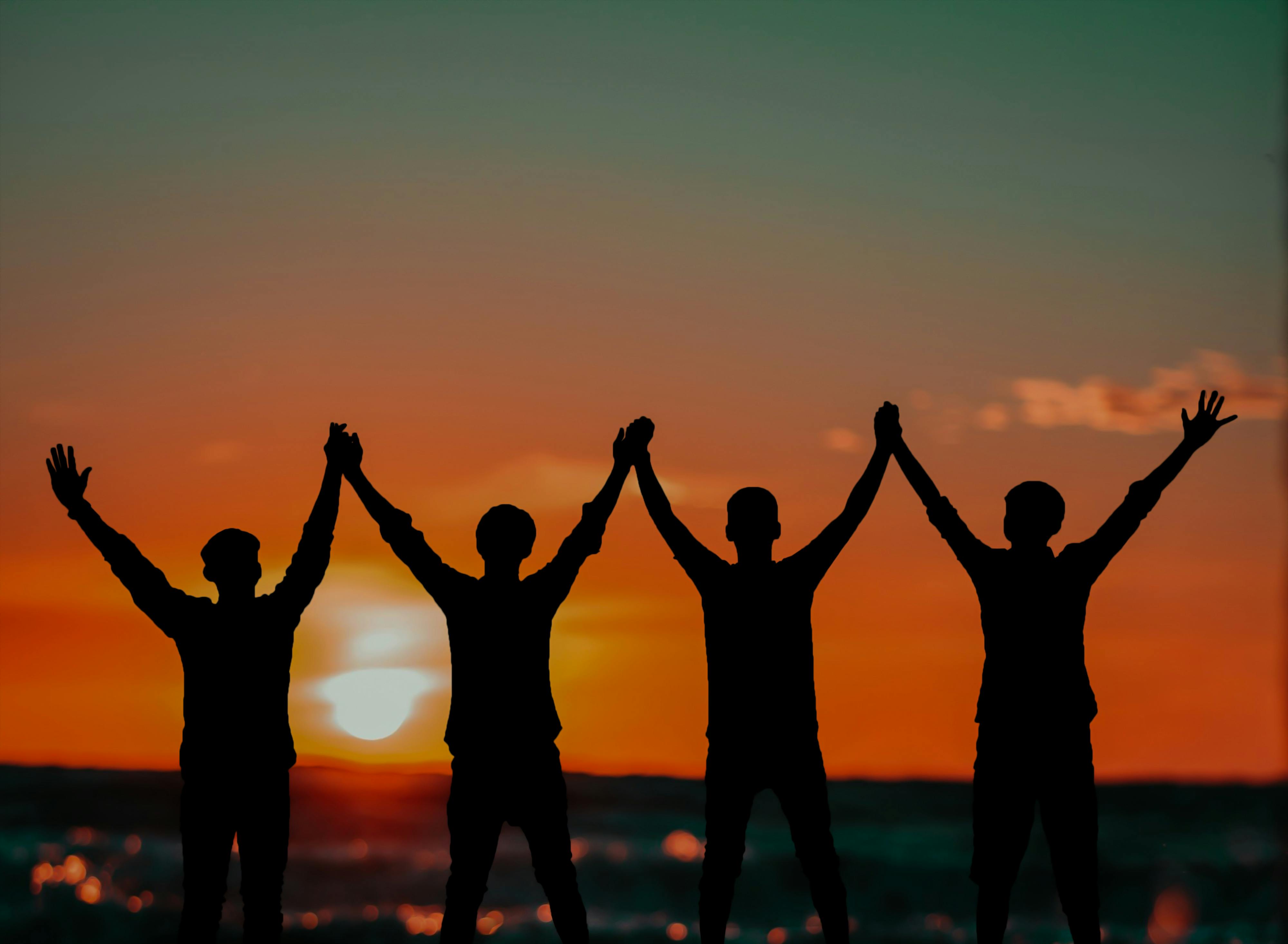 Silhouettes of four people holding hands at sunset, symbolizing unity and friendship.
